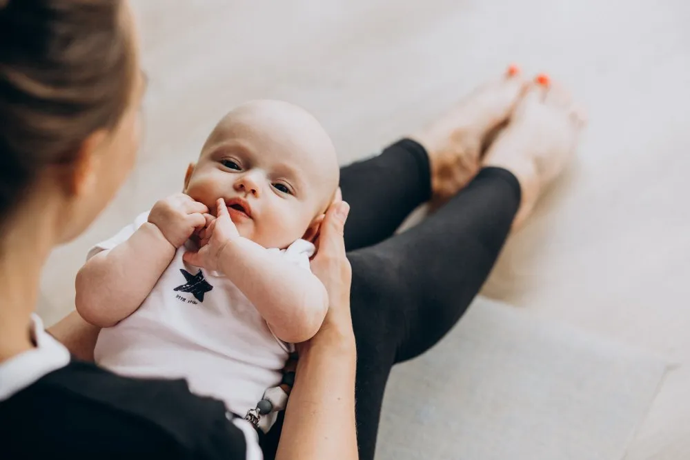 Mutter übt Yoga, ihr Baby liegt lachend vor ihr