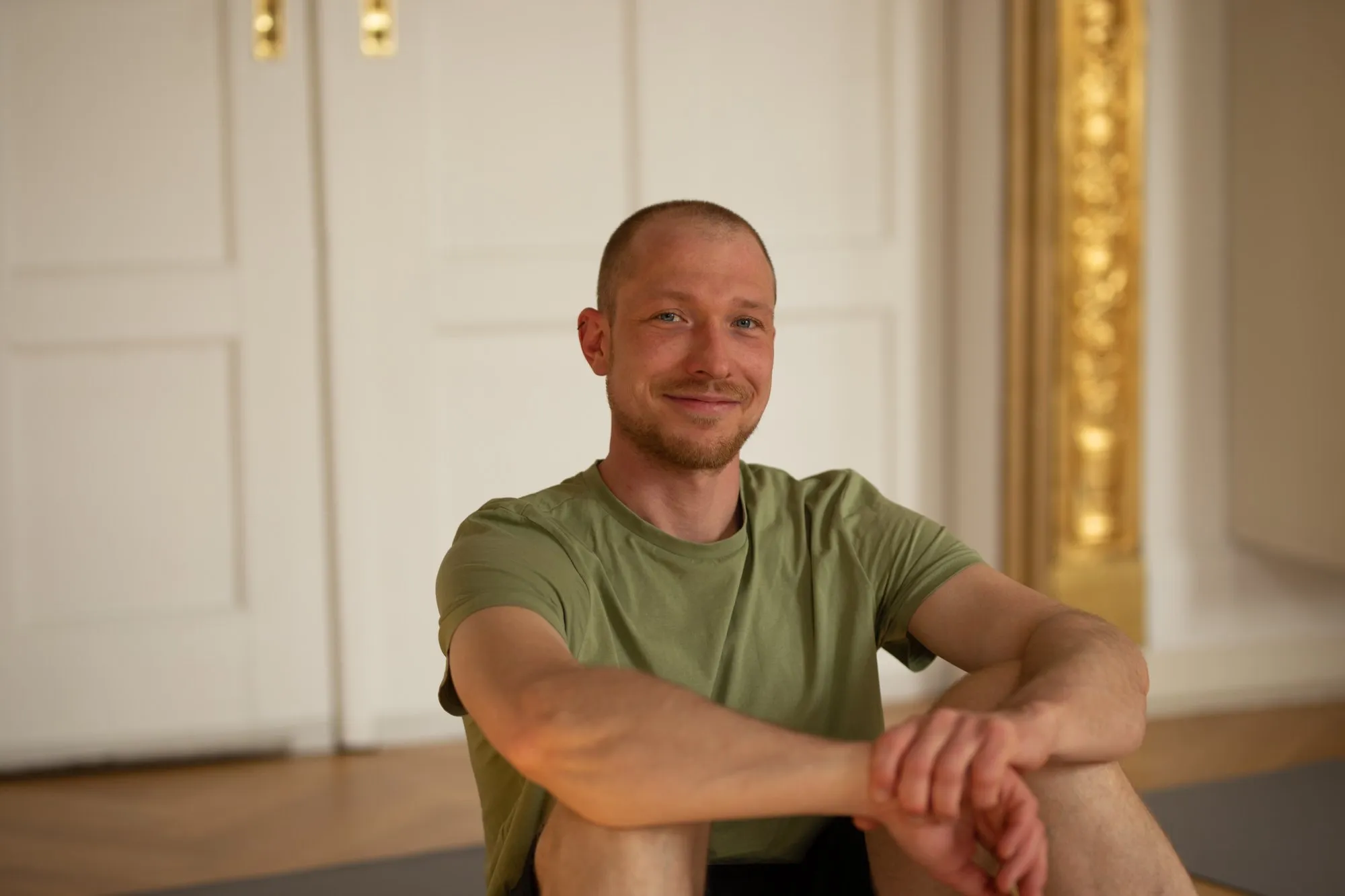Fabian sitzt lächelnd auf dem Boden eines hellen Yogaraums